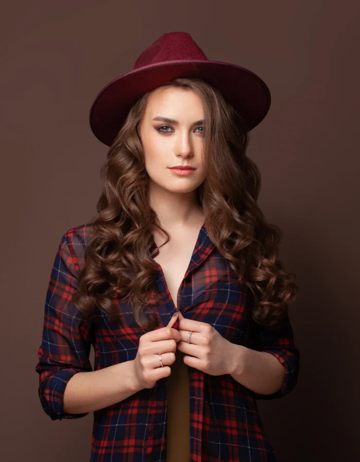 brunette-woman-plaid-shirt-fedora-hat-brown-background Custom Caps Manufacturer